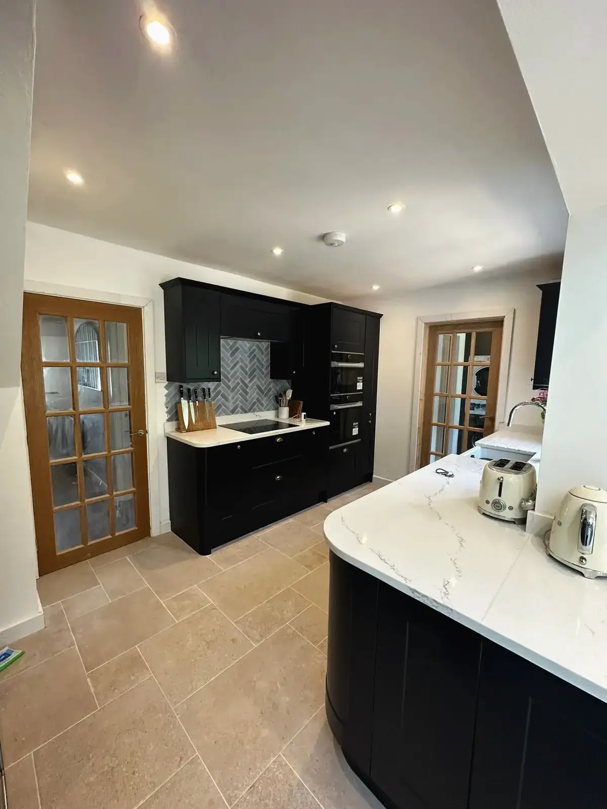 Bespoke kitchen refurbishment with black cabinetry and light stone flooring