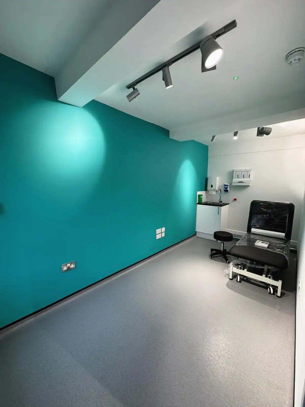 Clean consultation room with teal accent wall, medical bed, and spot lighting