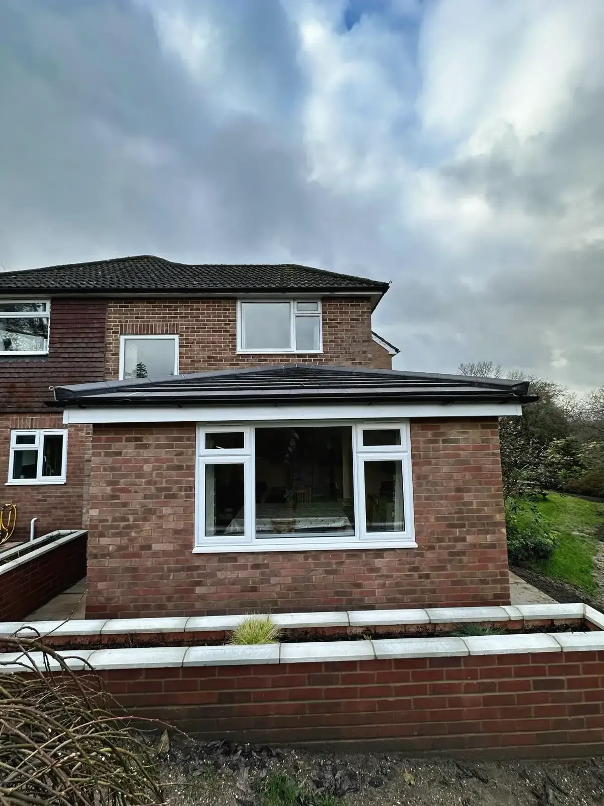 Close-up view of a brick house extension with white framed windows and planter wall