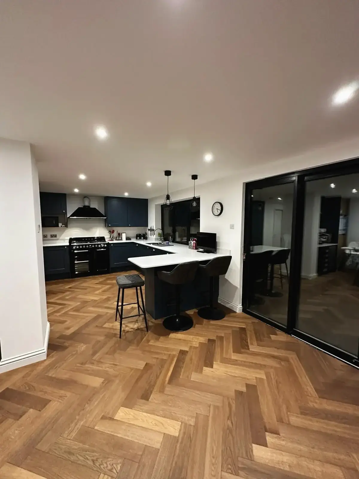 Elegant open kitchen with herringbone flooring and black-framed doors