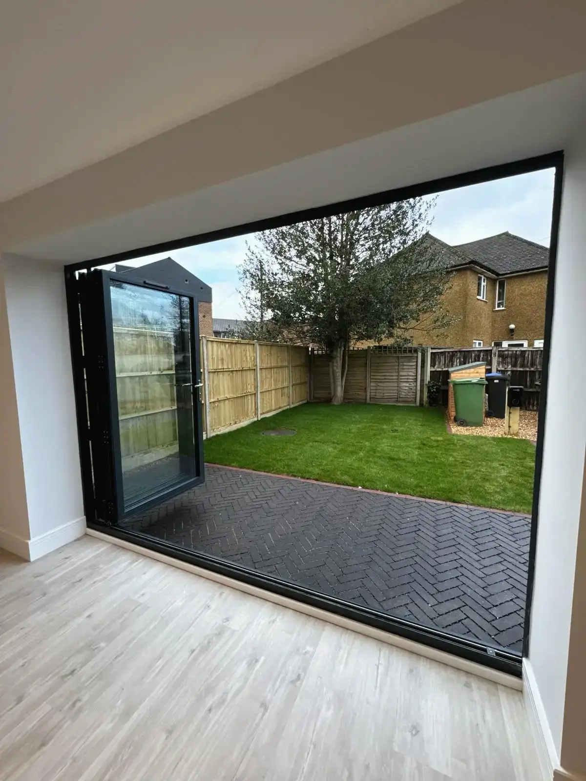 Large bi-fold glass doors opening to garden with lawn and paving