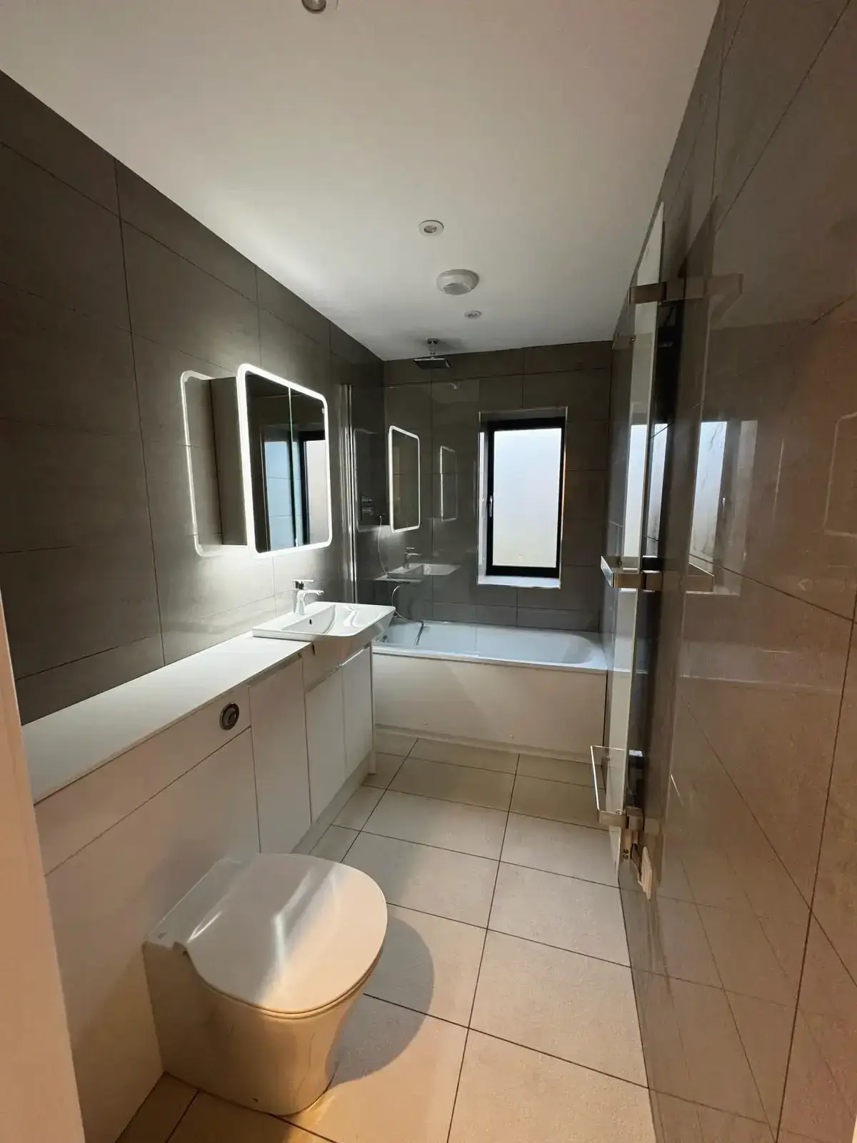 Luxury bathroom refurbishment with built-in vanity, bathtub, and frosted window by Godman Contruction