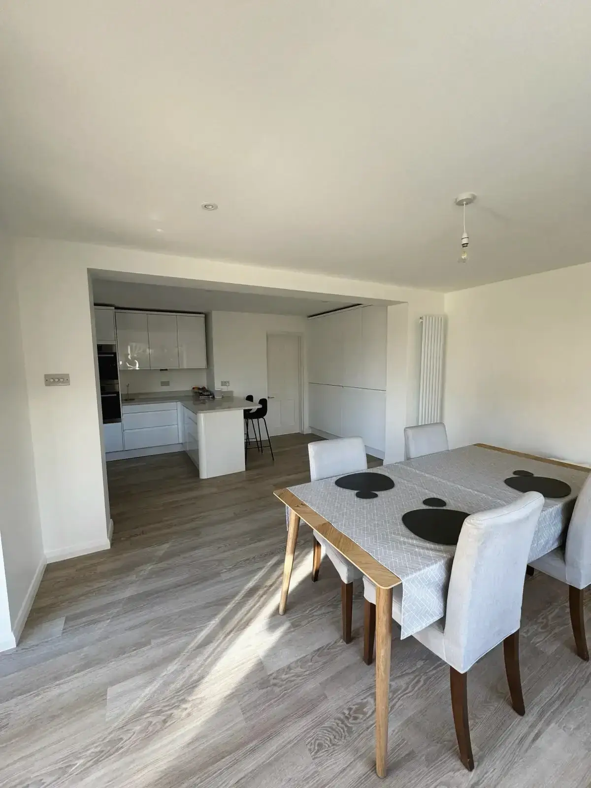 Modern dining room with table set, leading into contemporary white kitchen renovation