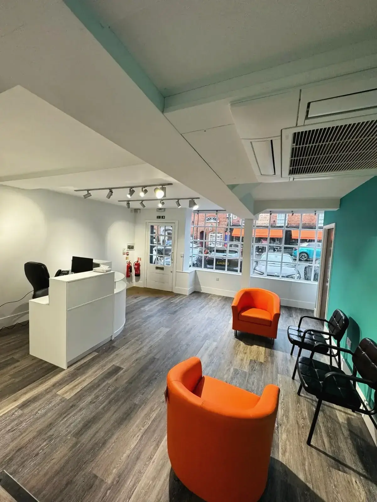 Reception waiting area with black chairs, teal accent wall, and wooden flooring