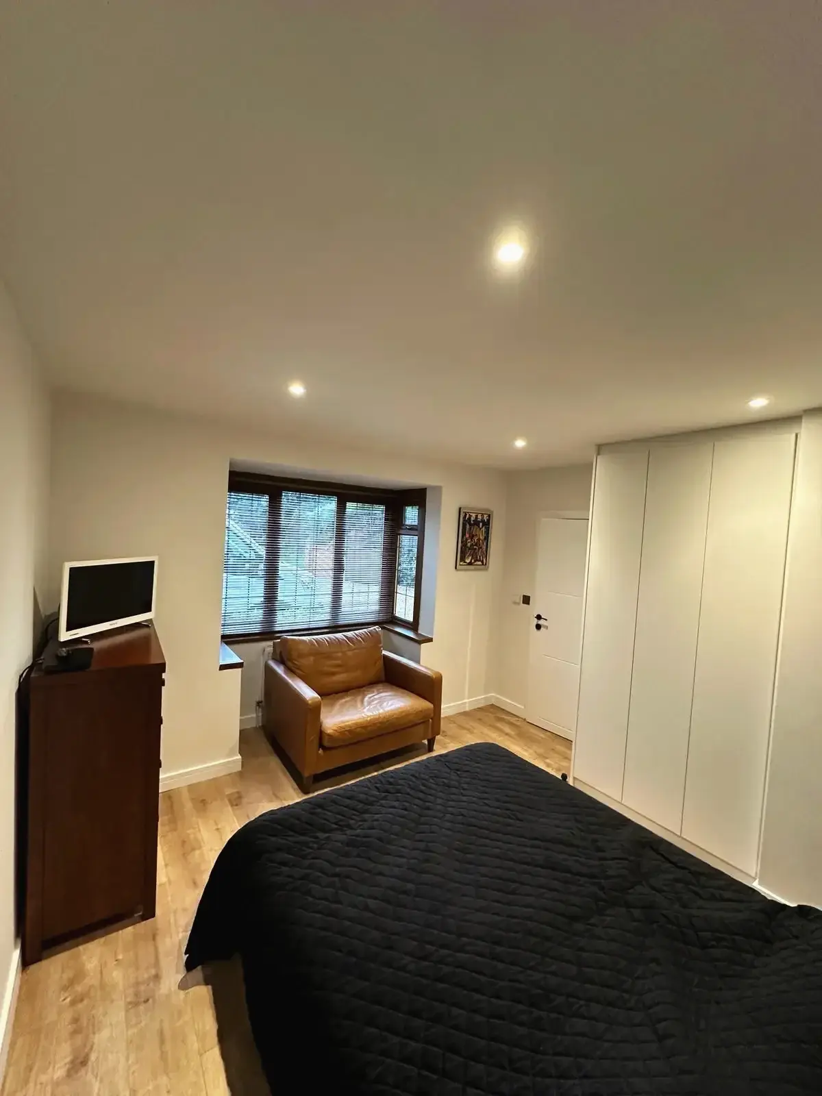 Renovated bedroom interior featuring wooden flooring, fitted wardrobes, and large window