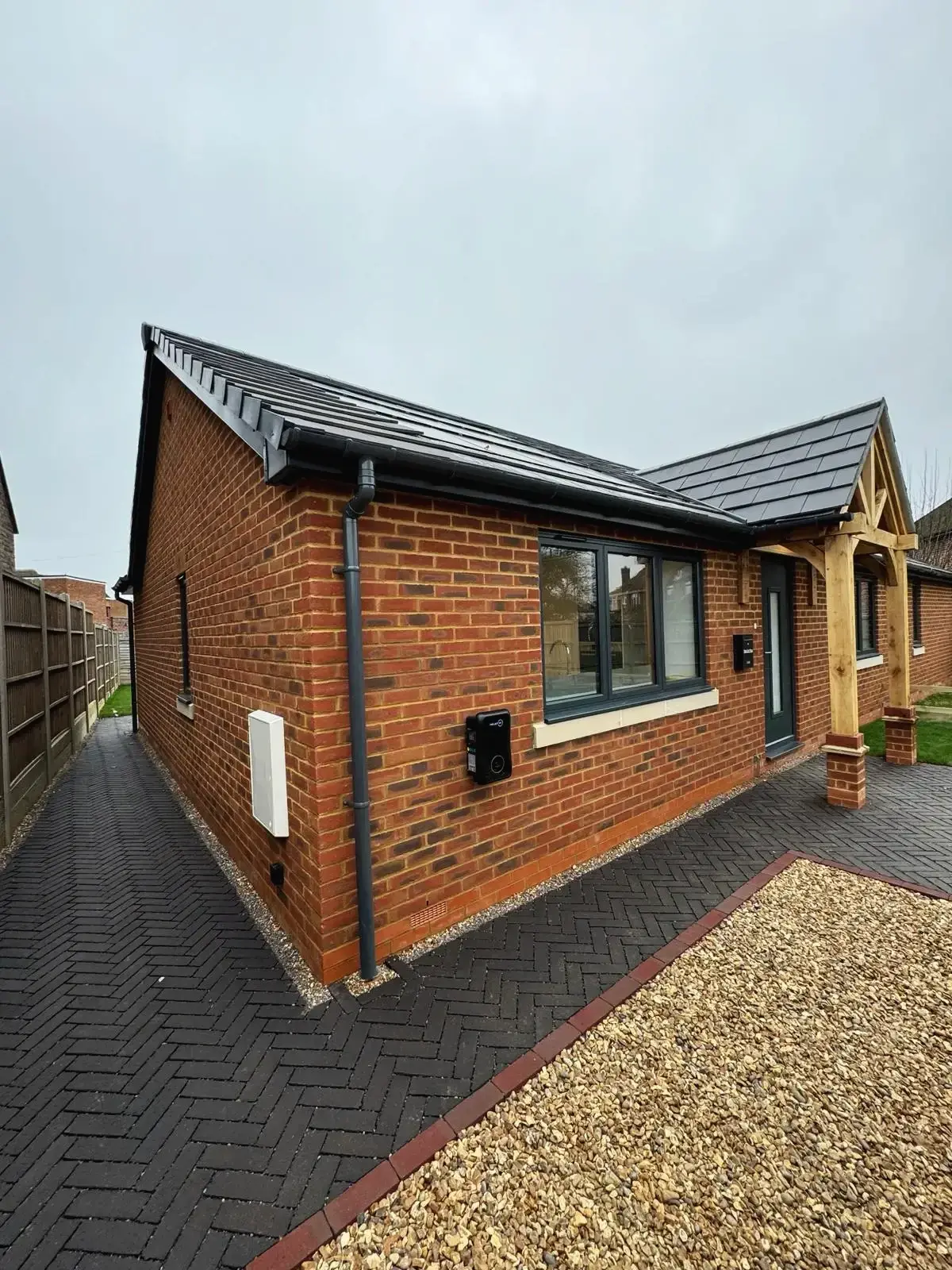 Side view of modern brick bungalow with paved pathway and oak porch