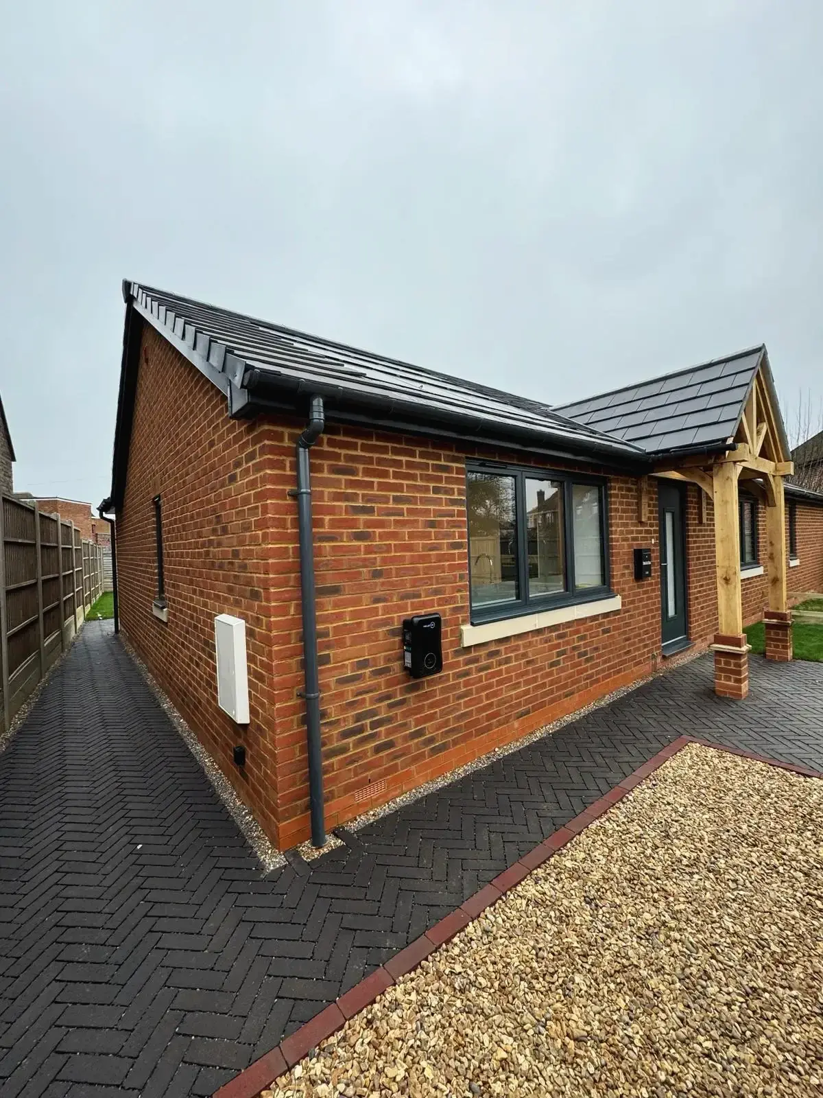 Side view of modern brick bungalow with paved pathway and oak porch