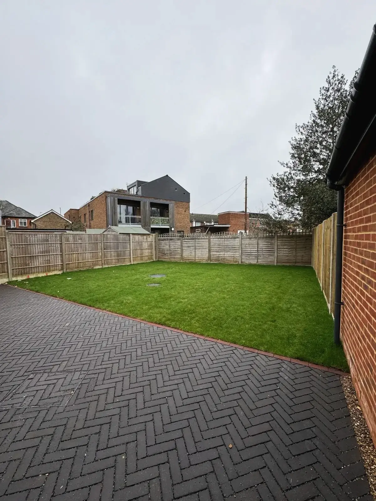 Spacious rear garden with paved patio and fenced boundary at modern home