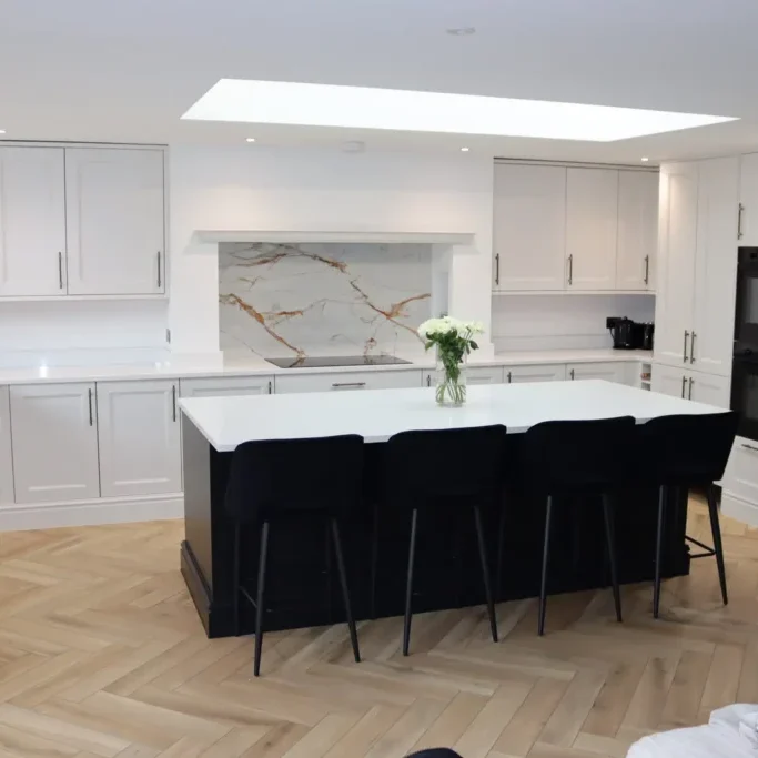 Modern open-plan kitchen design featuring white shaker cabinets, a large island, herringbone flooring and a skylight for natural light.