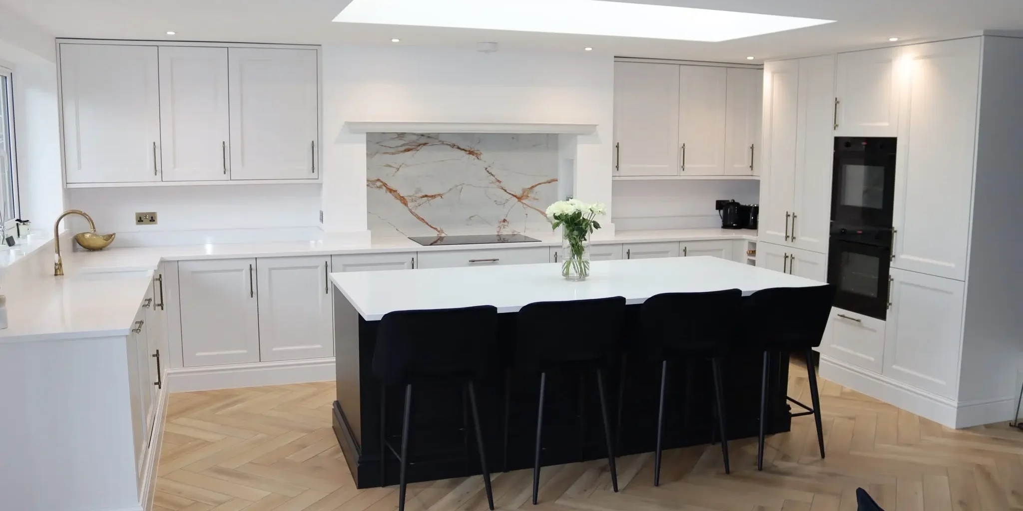 Modern open-plan kitchen design featuring white shaker cabinets, a large island, herringbone flooring and a skylight for natural light.